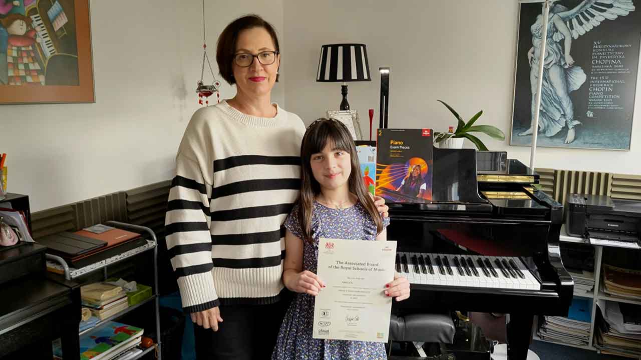 Anna Peszko presenting her pupil Adelyn with her ABRSM Grade 2 Distinction certificate.